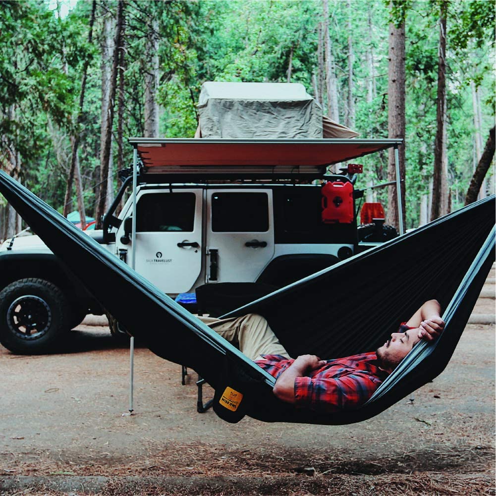 A man laying in a hammock next to a jeep.