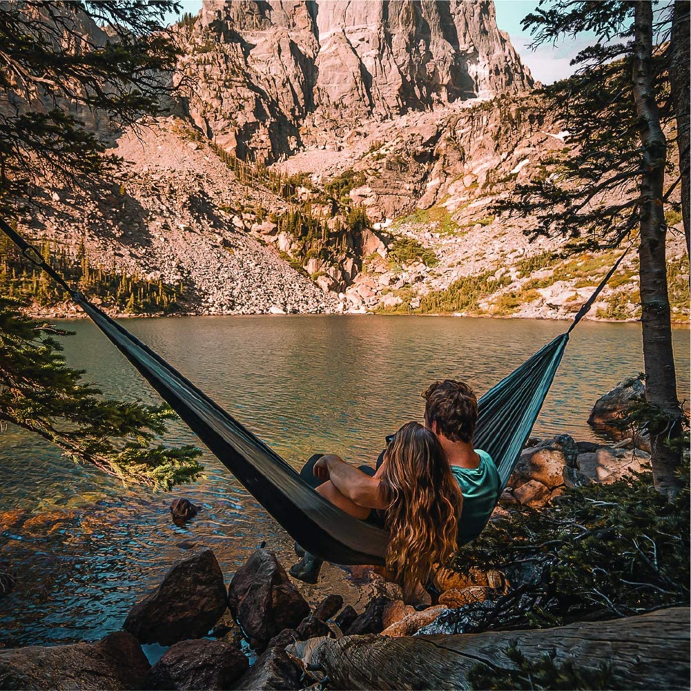 A man laying in a hammock next to some water