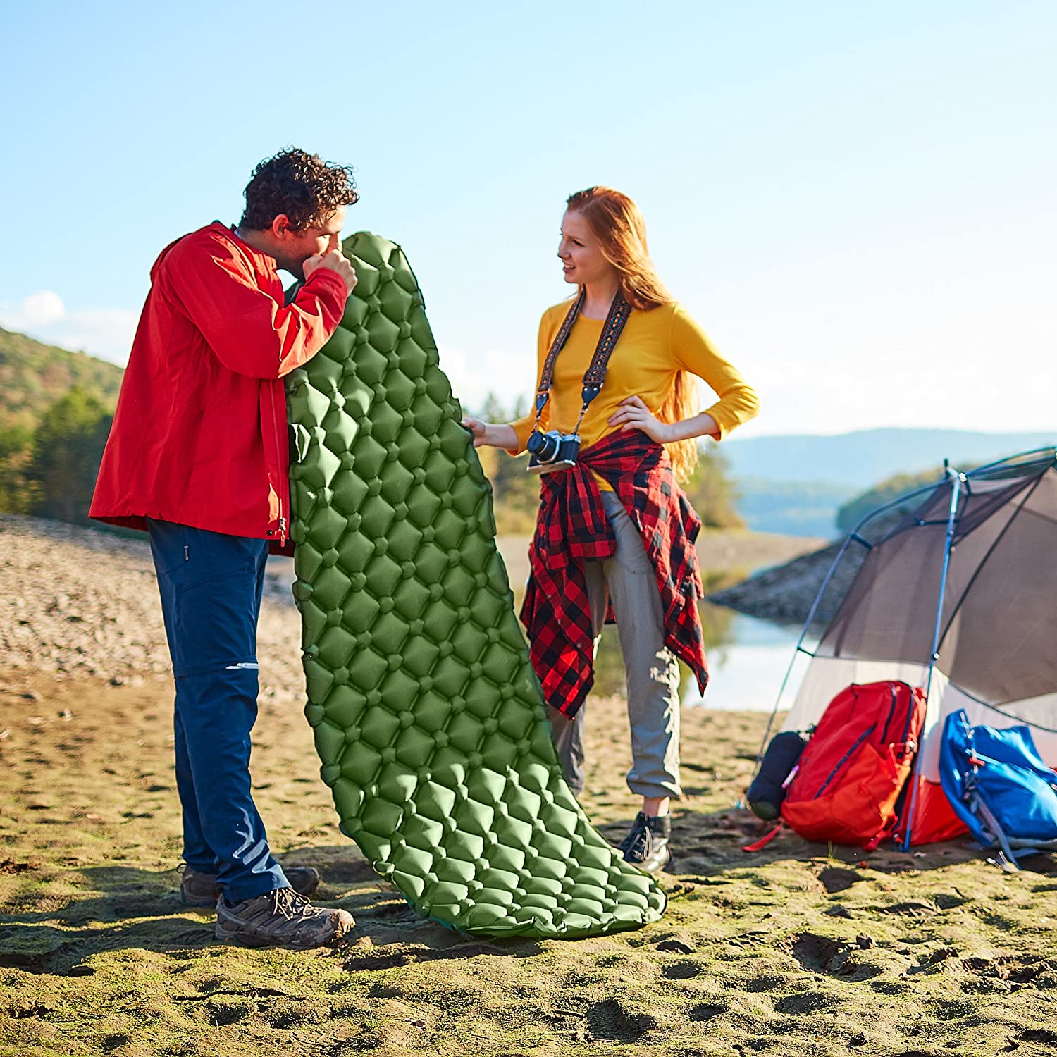 A man and woman standing on the beach near an inflatable mattress.